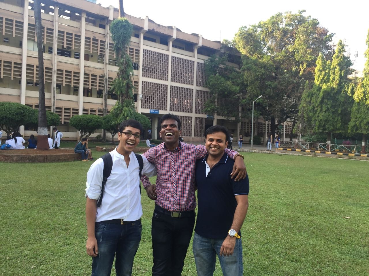 Three friends standing on a campus lawn in front of a building