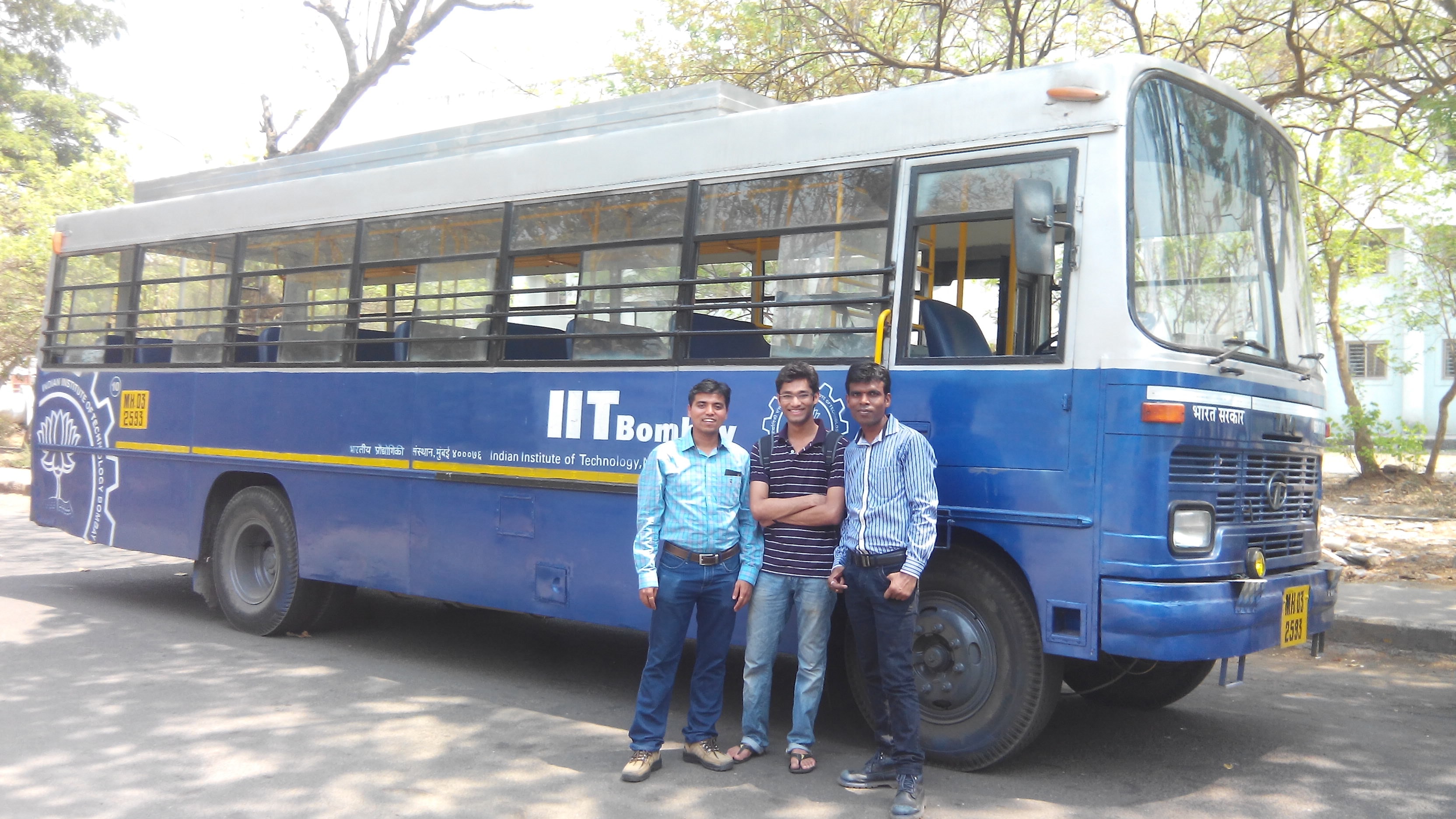 Three friends standing beside an IIT Bombay campus bus